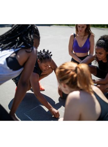 An athlete is drawing on the ground with a piece of chalk, her team mates are watching her explain something. 